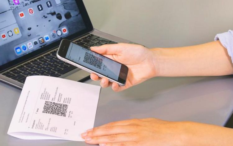 Eine Frau erfasst mit dem Handy den QR-Code einer QR-Rechnung