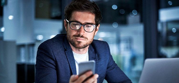 Geschäftsmann im Büro schaut auf sein Handy