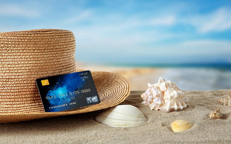 Strohhut am Strand mit Kreditkarte und Muscheln im Sand